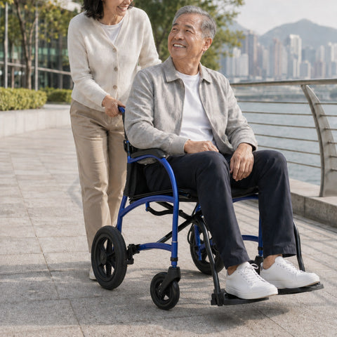 A woman pushes an older man seated upright in his blue Strongback Excursion transport chair along a waterfront promenade